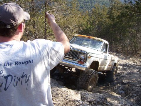 1999 Jeep TJ - A white Jeep pickup truck tackles a challenging off-road trail, with a person in the foreground.
