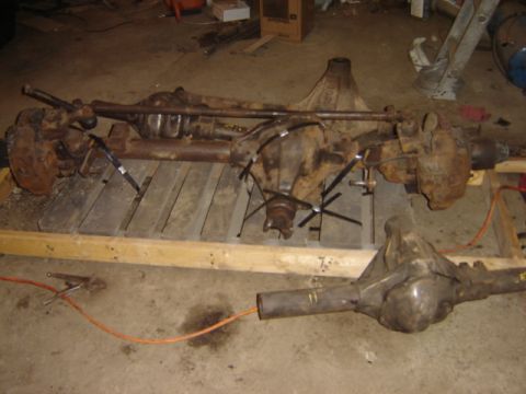 1992 Ford Bronco - Two old, rusty vehicle axles are resting on wooden pallets in a workshop setting.
