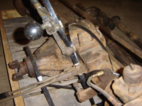 1992 Ford Bronco - Close-up view of a rusty differential assembly, a chrome shifter knob and metal lever, with driveshafts in the background.