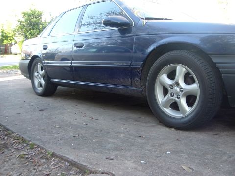 1993 Ford Taurus - This blue sedan is parked on a concrete surface with some leaves and debris scattered around.