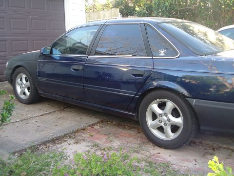 1993 Ford Taurus - This 1993 Ford Taurus sedan is seen from the side, a dark blue paint job and aftermarket wheels.