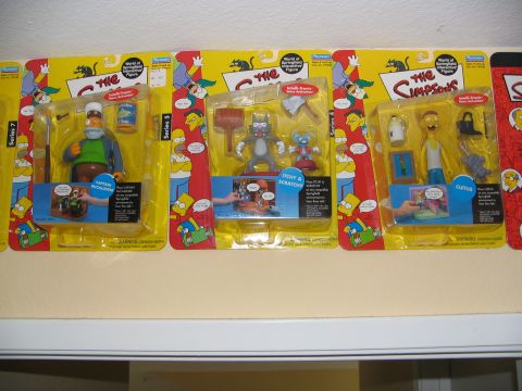 1994 Ford Crown Victoria - A collection of The Simpsons action figures are displayed in their original packaging on a shelf.