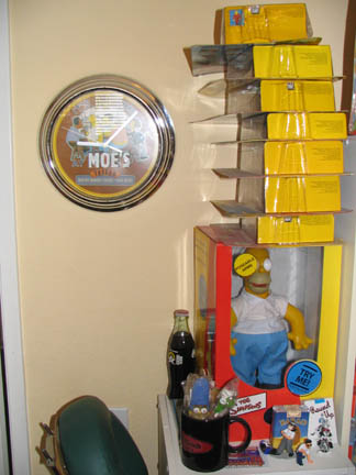 1994 Ford Crown Victoria - A wall clock with 'Moe's' on it hangs near a stack of boxes and a Homer Simpson doll.
