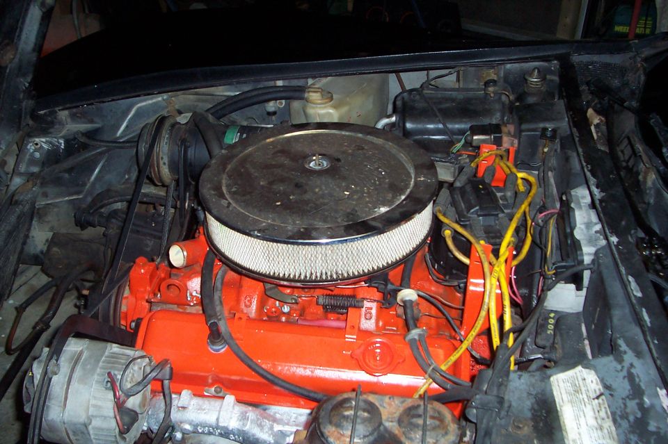 Orange-painted Chevy V8 engine with chrome air cleaner and yellow plug wires in a 1975 Corvette engine bay
