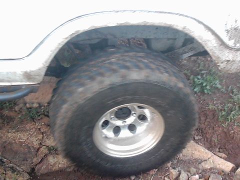 1978 Ford Bronco - A white vehicle navigates rough terrain, showing its wheel and fender in close-up.