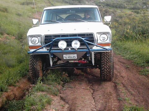 1978 Ford Bronco - A white 1978 Ford Bronco with off-road modifications navigates a dirt trail.