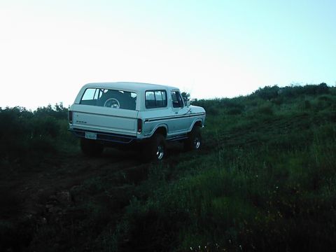 1978 Ford Bronco - A 1978 Ford Bronco navigates a muddy, grassy incline under a clear sky.