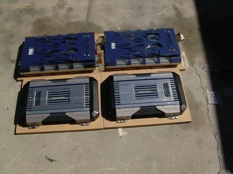 1995 Ford Contour - Four car audio amplifiers laid out on MDF boards on a concrete floor: two blue Kenwood units with flame-cut graphics and green LED indicato…