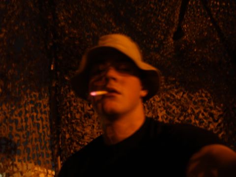 1988 Ford Bronco - A person wearing a bucket hat and smoking a cigarette is visible in the foreground, with a camouflage pattern in the background.