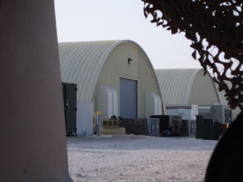 1988 Ford Bronco - Two large, arched military hangars are visible with various containers and equipment in front of them.