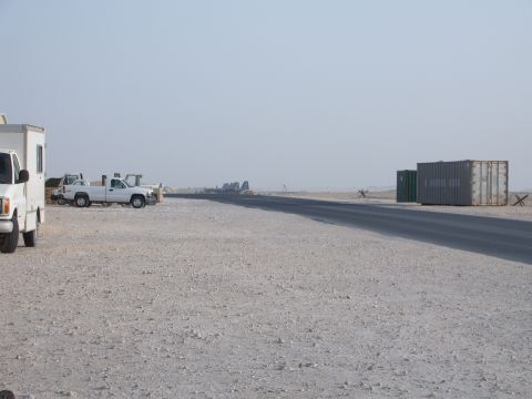 1988 Ford Bronco - Several white vehicles are parked in an open, dusty area with shipping containers visible in the distance.