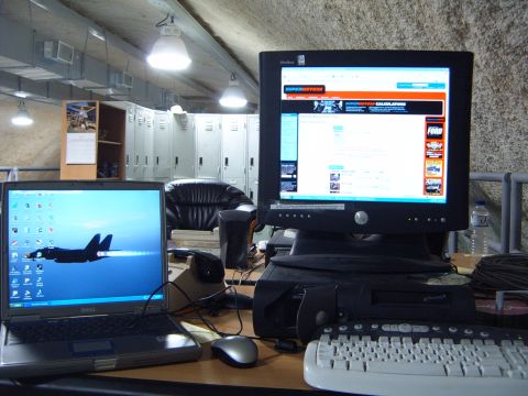 1988 Ford Bronco - A desk setup features two computers, one displaying a jet and the other a website, with lockers visible behind.