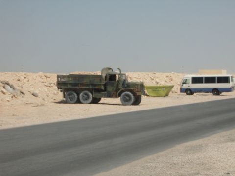1988 Ford Bronco - A military truck and a bus are parked in a desert landscape.
