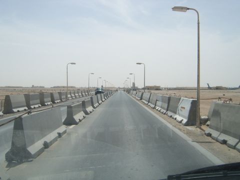 1988 Ford Bronco - A long, straight road stretches into the distance, flanked by concrete barriers and streetlights under a hazy sky.