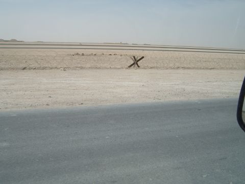 1988 Ford Bronco - A desolate desert scene barbed wire and anti-tank obstacles, with a road in the foreground.