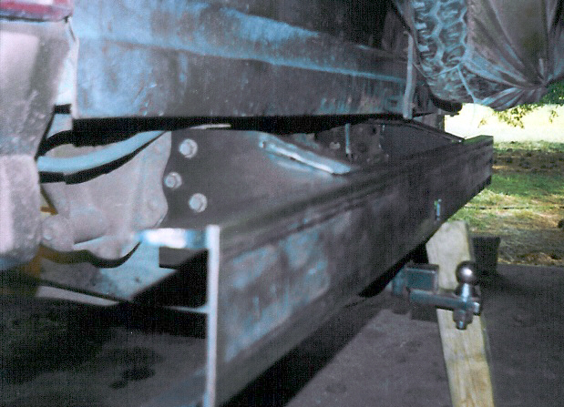 Underside view of a vehicle frame, leaf spring and rear axle on a jack stand and wood block