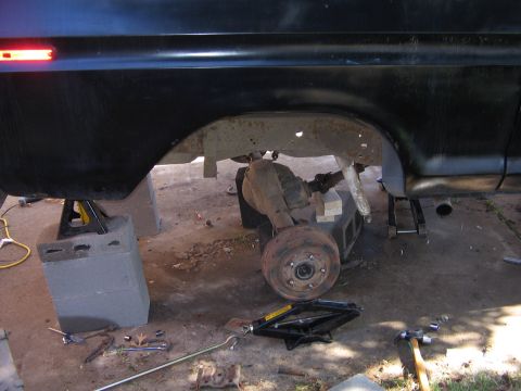 1978 Ford Bronco - The rear axle of a black SUV is visible, undergoing maintenance with the vehicle raised on jack stands.