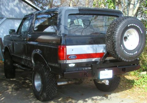 1988 Ford Bronco - Rear three-quarter view of a black Ford Bronco full-size SUV with a soft top, lifted suspension, and a rear-mounted spare tire with BFGoodr…
