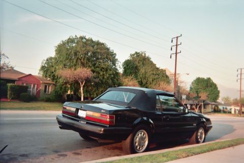 1985 Ford Mustang - A black 1985 Ford Mustang convertible is parked on the side of a street in a residential neighborhood.
