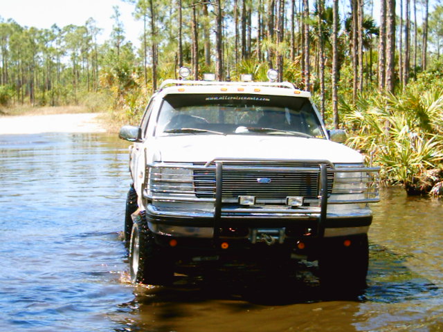 Lifted white Ford Bronco with grille guard and roof lights standing in deep water on a sand trail