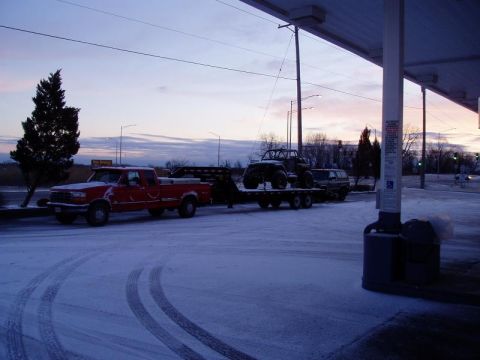 1992 Ford Bronco - A red pickup truck tows a trailer with a UTV and SUV through a snowy landscape at dusk.
