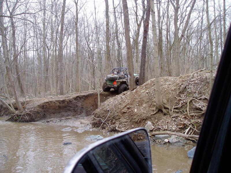 Off-road vehicle climbing dirt embankment in woods; Supermotors.net logo visible