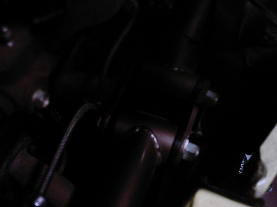 Close-up of a dark-colored vehicle suspension part with bolts and a braided hose