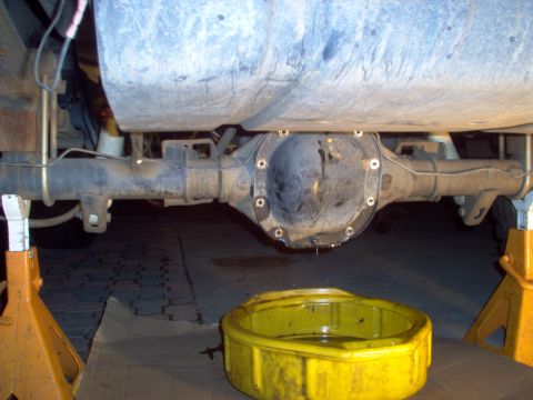 1988 Ford Bronco - The underside of a vehicle shows a rear differential being serviced, with old fluid draining into a pan.