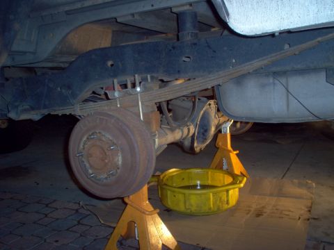 1988 Ford Bronco - Vehicle's rear axle and differential are raised on jack stands for maintenance, with a drain pan ready.