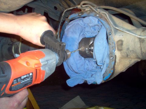 1988 Ford Bronco - A person drills into a vehicle's differential housing, which is covered with a blue cloth.