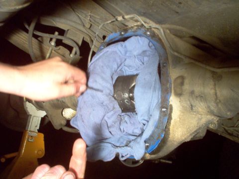 1988 Ford Bronco - A person is working on the rear differential of a vehicle, with a blue cloth stuffed inside.