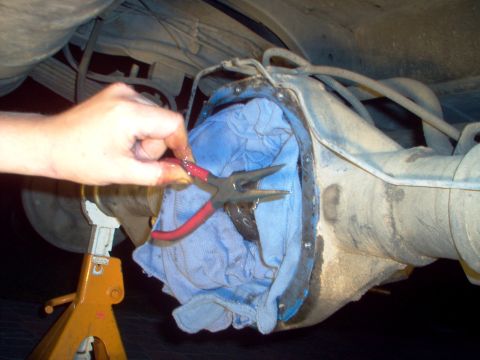 1988 Ford Bronco - A hand uses pliers to remove a differential cover during a vehicle repair.