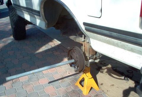 1988 Ford Bronco - The rear suspension and axle of a white truck are visible, supported by yellow jack stands.