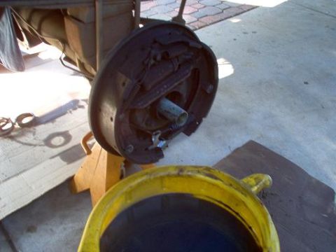 1988 Ford Bronco - A rear differential brake drum assembly is shown on a jack stand, with a yellow drain pan in the foreground.