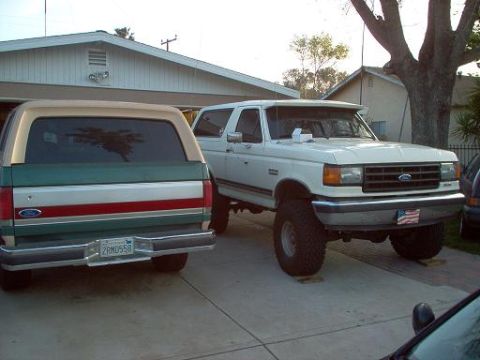 1988 Ford Bronco - A white Ford Bronco with a lifted suspension and aftermarket grille is parked in a driveway next to another SUV.