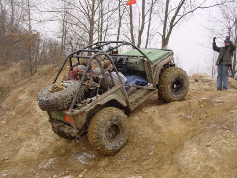 1992 Ford Bronco - An off-road buggy navigates a steep, muddy incline with a person watching from the top.