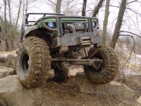 1992 Ford Bronco - This heavily modified off-road vehicle navigates a rocky terrain with its large, mud-caked tires.