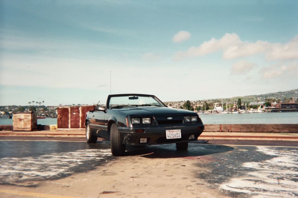Black convertible parked by a harbor, front view. License plate reads 4GYU651