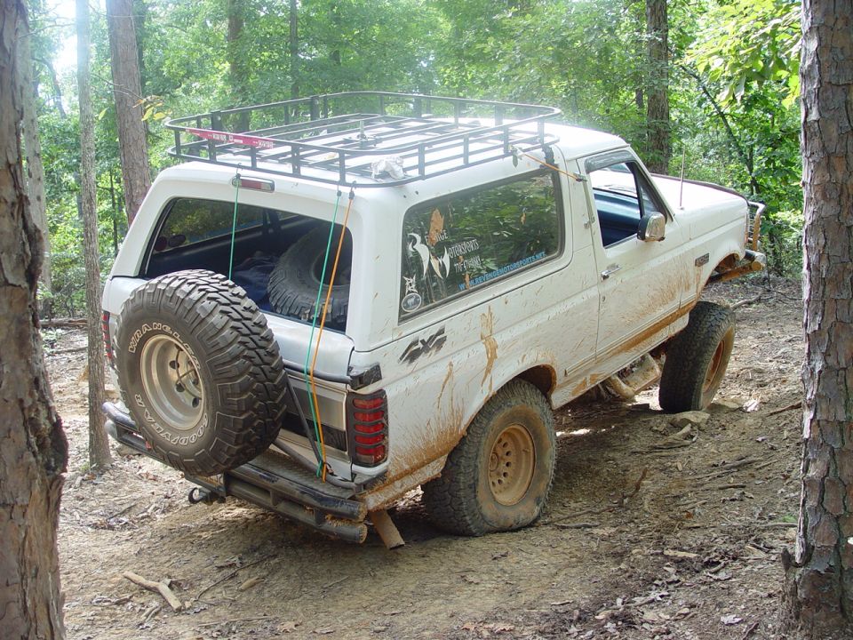 Rear of white Ford Bronco with roof rack and tailgate-mounted spare tire on a trail