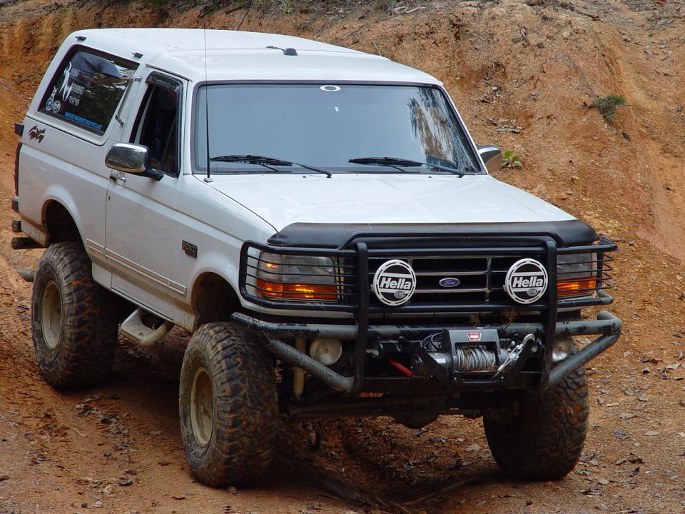 White Ford Bronco with brush guard, Hella lights and winch parked on a red-dirt bank
