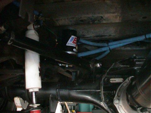 1979 Ford Bronco - Close-up view of underbody suspension parts, including a white shock absorber and blue hoses, with visible text on a black component.