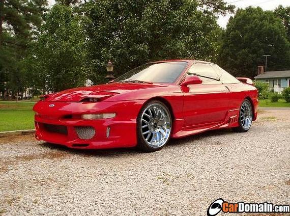 Red Ford Probe with body kit and chrome wheels parked on a gravel lot