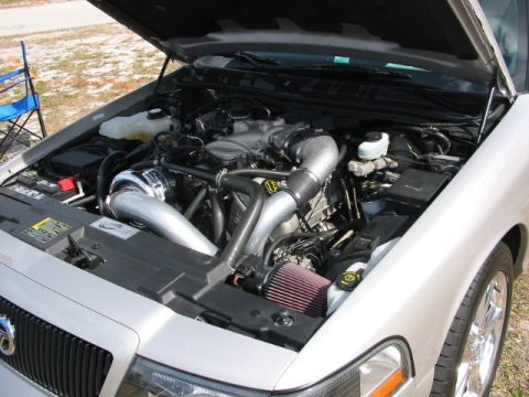 1997 Ford Crown Victoria - The engine bay of a silver sedan, modified with a turbocharger and custom intake, is shown with the hood open.