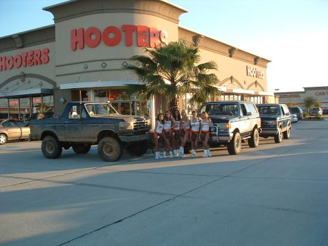 1993 Ford Bronco - Three Ford Broncos are lined up in front of a Hooters restaurant, with a group of women standing between the first two vehicles.