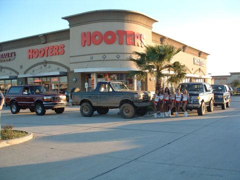 1993 Ford Bronco - Three Ford Bronco SUVs are parked outside a Hooters restaurant, with a group of women posing for a photo.