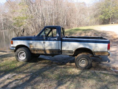 1989 Ford F-150 - This lifted Ford F-150 pickup truck is shown from the side, with a two-tone paint scheme and off-road tires.
