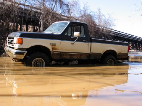 1989 Ford F-150 - This two-tone pickup truck appears to be stuck in muddy water, with a bridge in the background.