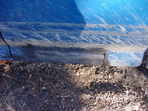 1993 Ford F-150 - Mud-splattered blue truck side panel with black trim, viewed from a low angle near the ground.