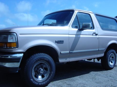1996 Ford Bronco - A tan 1996 Ford Bronco is shown from a 3/4 front angle against a blue sky.