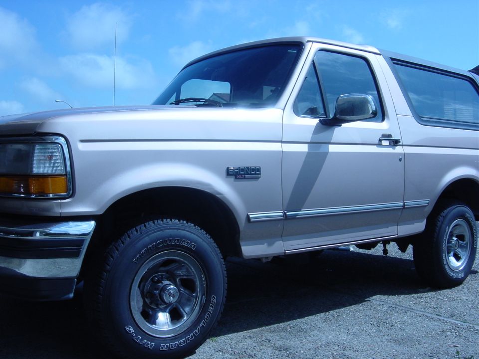 Tan 1996 Ford Bronco with chrome trim and a "BRONCO" badge on the fender, viewed from the front 3/4 angle